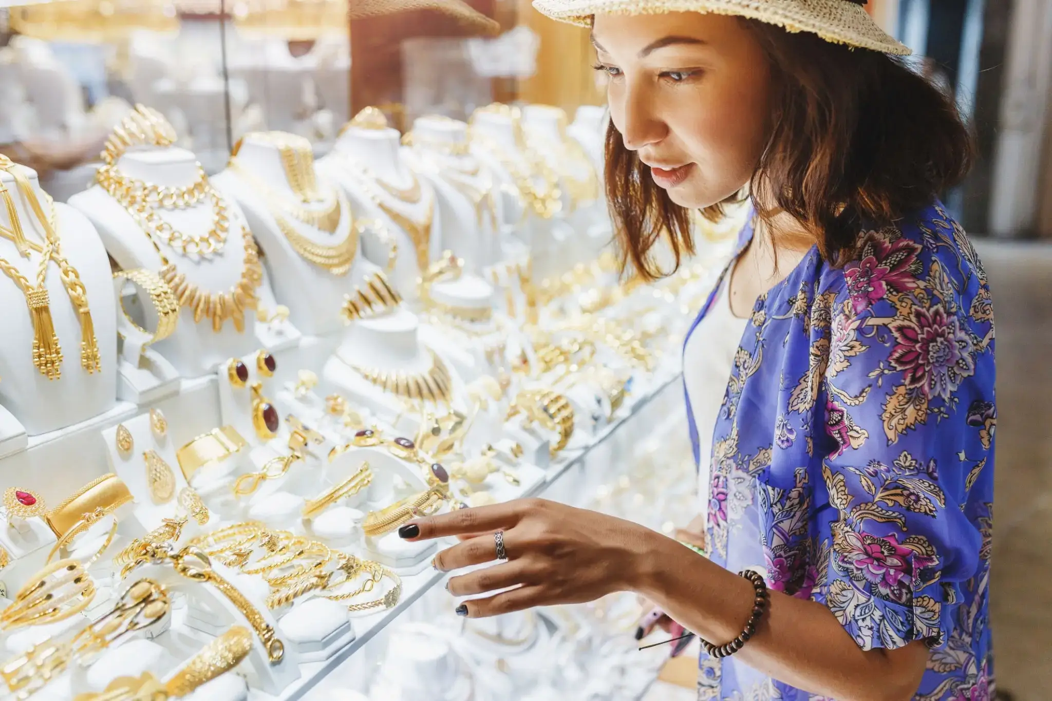 A woman admires gold jewelry displayed in a shop window.