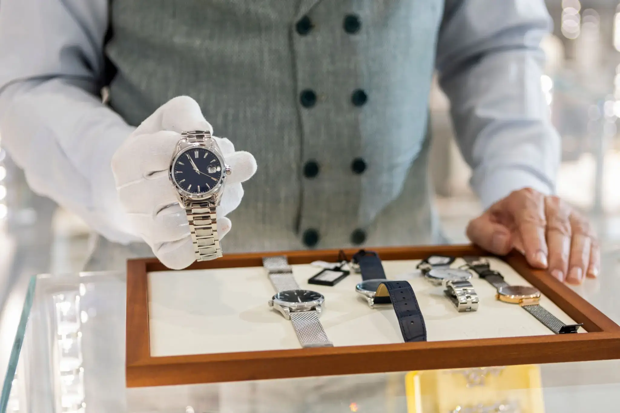 A person in a vest displays a luxury wristwatch with multiple watches on a tray.
