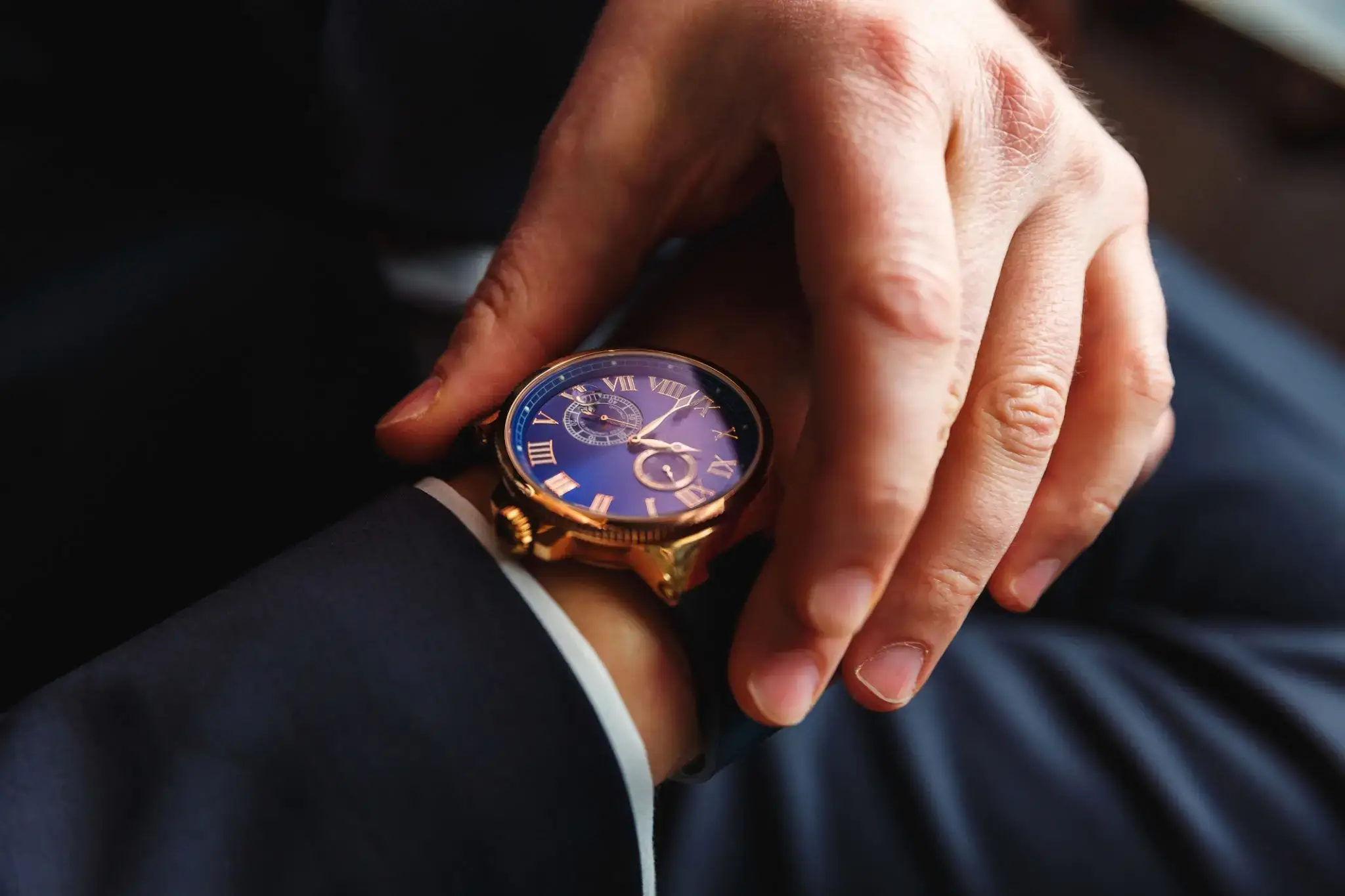 Close-up of a hand adjusting a luxury wristwatch on a suit sleeve.