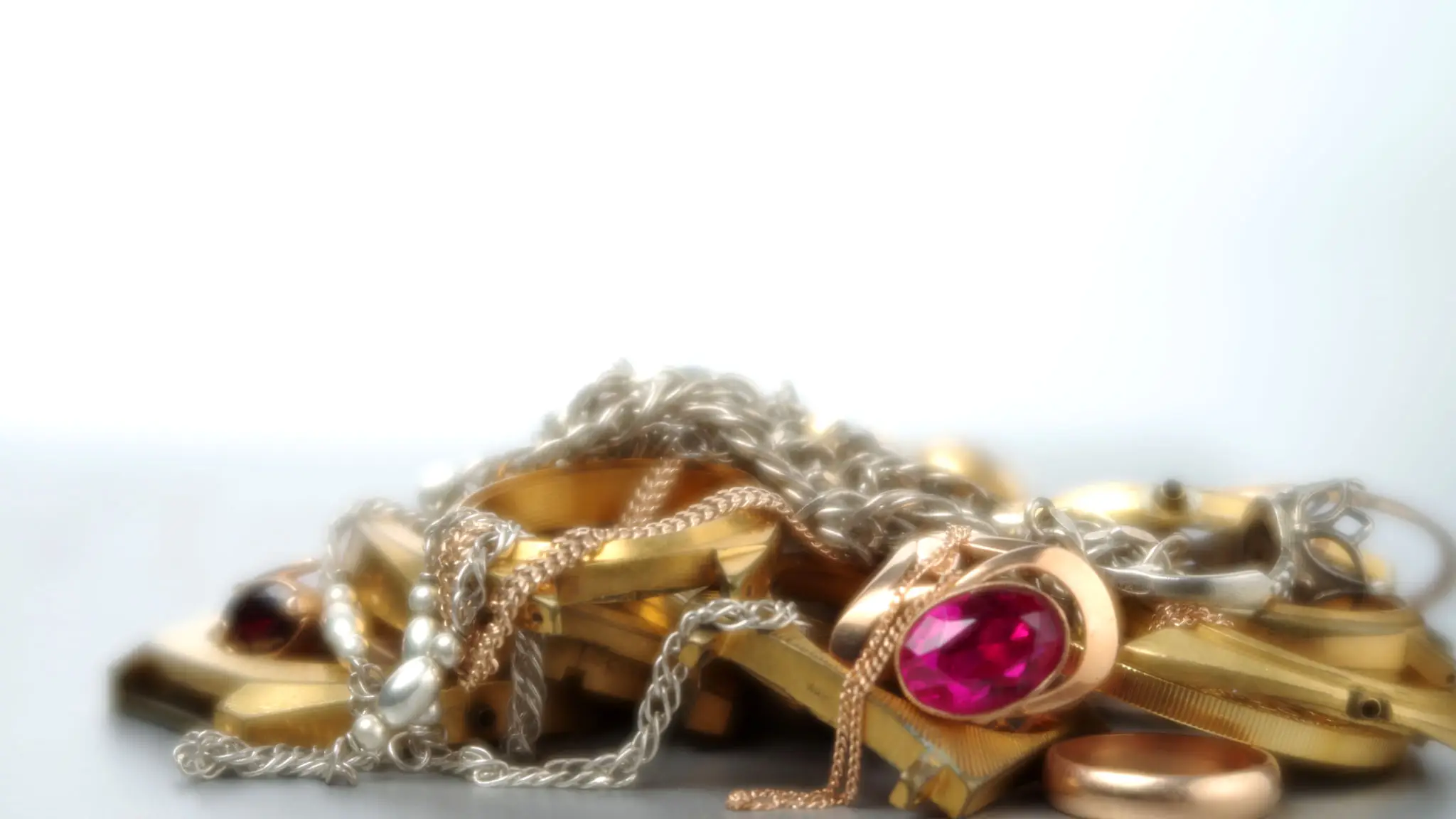 Close-up of a gold ring with a pink gemstone on a tangled silver chain.